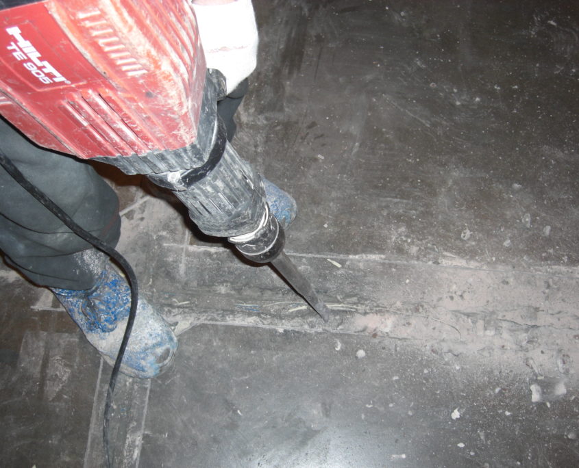 Person using a hand held machine to chip away at the damaged floor