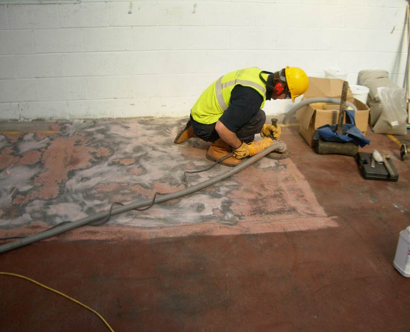 Man removing paint and dirt using a hand held diamond grinder so that coatings and screeds can be applied