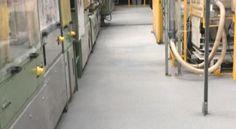 A factory or industrial workspace featuring machinery, equipment, and pipes lining both sides of a clean, empty aisle.