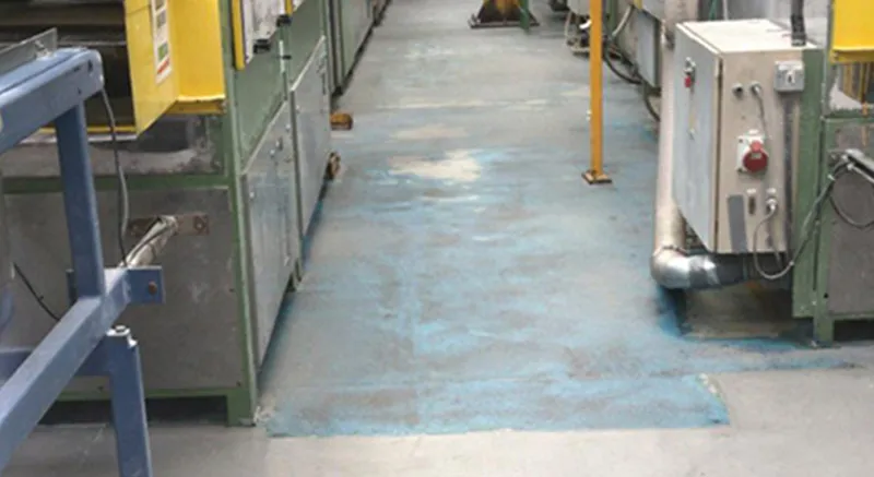 A factory or industrial facility walkway with faded blue paint on the floor, flanked by machinery, control panels, and safety railings on both sides.
