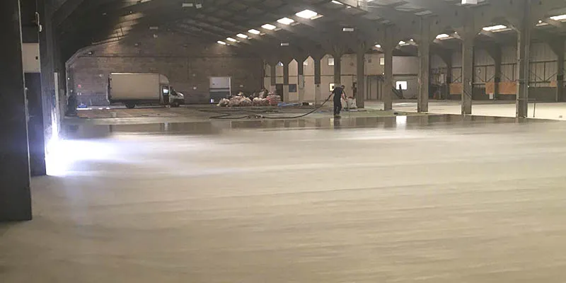 Workman laying rapid pumped screed in a large industrial warehouse space.