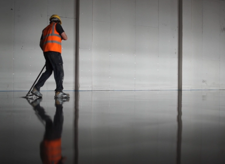 Workman laying pumped screed in a warehouse space.
